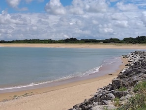 A beach with a rocky shoreline, calm water, and a distant tree line. - Beautiful villa 5 minutes from the beach. Pets welcome. (PLAISANCE)