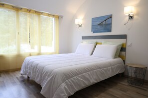 Une chambre à coucher avec un lit, une fenêtre avec des rideaux, une lampe fixée au mur et un tableau.