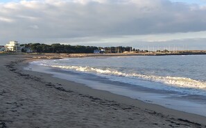Une plage avec un rivage sablonneux, des vagues et un bâtiment à la façade blanche en arrière-plan.