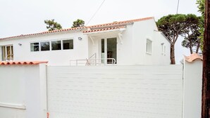 Un bâtiment blanc avec un toit recouvert de tuiles et une entrée fermée par un portail.