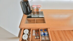 A wooden drawer unit with compartments containing a coffee maker, two cups, a spoon, a napkin, and two bottles of water. - Prague Saigon Airport Hotel (Ho Chi Minh City)