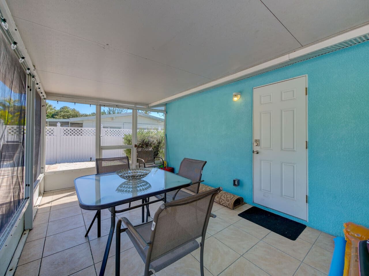 A covered patio area with a glass table and chairs, a white door, and a blue wall.
