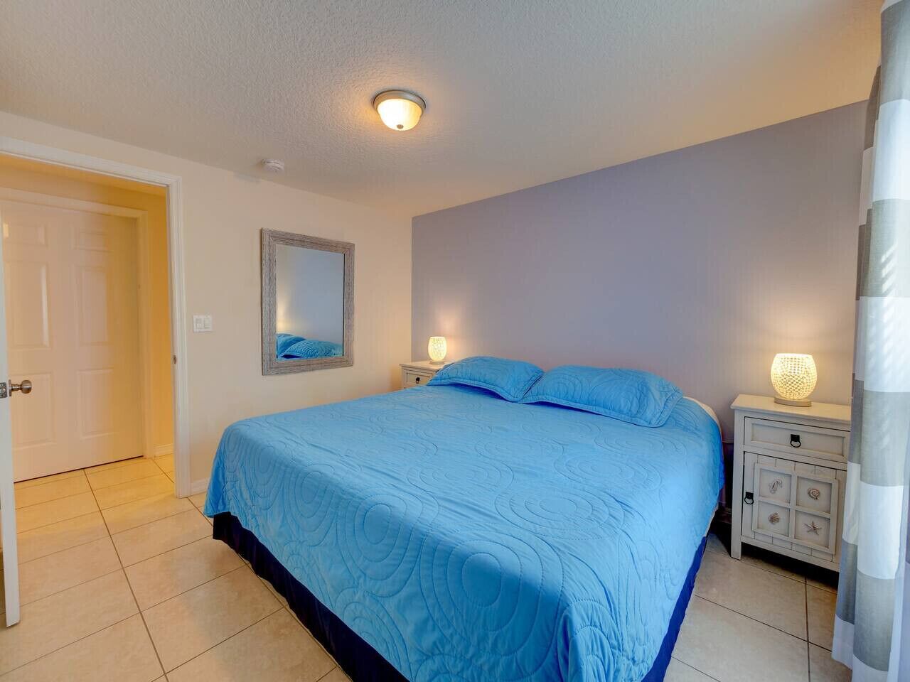 A bedroom with a large bed, a nightstand, a mirror, and a door.