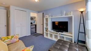 Una sala de estar con sofá, televisor, mesa de centro y una kitchenette al fondo.