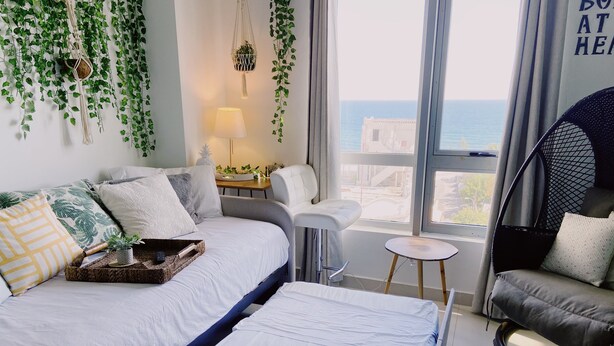 Un dormitorio moderno con una cama, una mesita pequeña, una silla y una planta de macramé colgante.