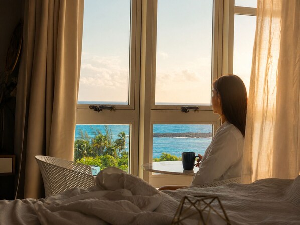 Ein Zimmer mit Bett, einem Fenster mit Meerblick und einer Tasse auf dem Fensterbrett.