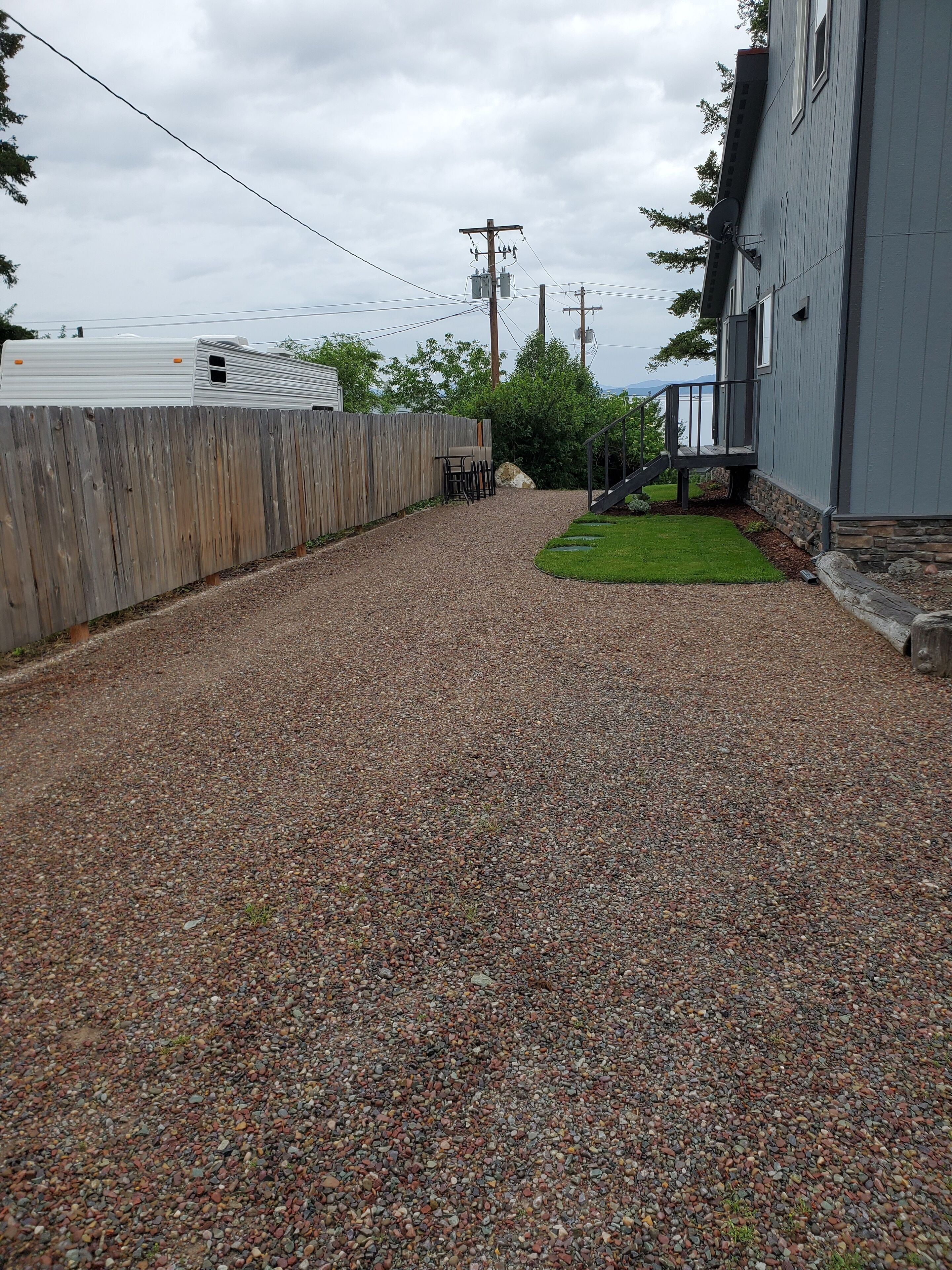 A gravel driveway leading to a house with a wooden fence, a satellite dish, and a stone wall.