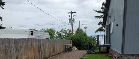 A gravel driveway leading to a house with a wooden fence, a satellite dish, and a stone wall.