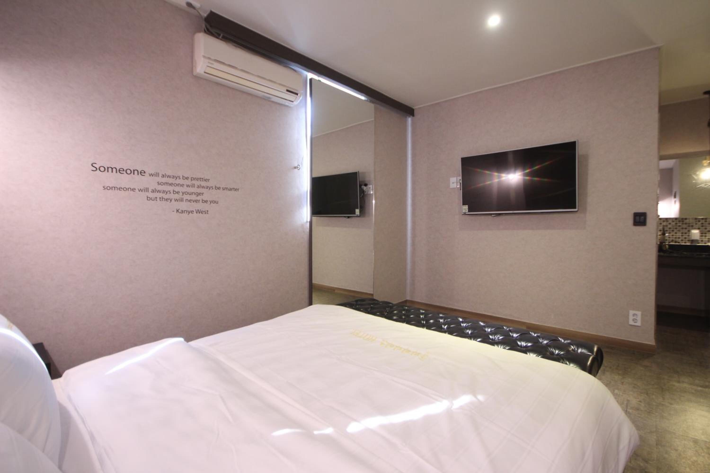 Habitación de hotel con cama, televisor de pantalla plana montado en la pared y un espejo que refleja parte de la habitación.