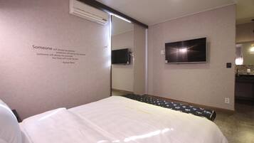Habitación de hotel con cama, televisor de pantalla plana montado en la pared y un espejo que refleja parte de la habitación.