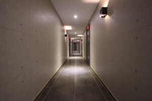 Un pasillo largo y estrecho con pisos y paredes de baldosas, equipado con letreros de salida de emergencia e iluminación.
