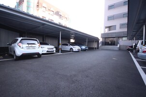 Un estacionamiento con varios coches, un paseo techado y un edificio de varios pisos con balcones.