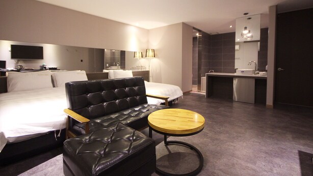 Et moderne hotelværelse med en stor seng, en lædersofa, et lille rundt bord, et fjernsyn og et separat badeværelse.