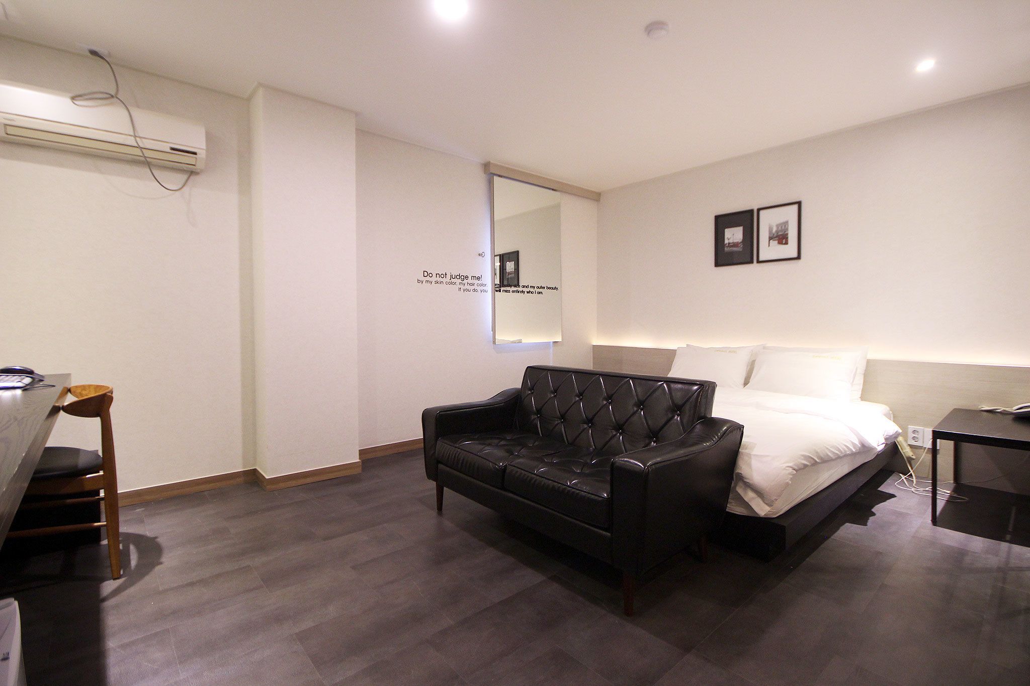 Un dormitorio con cama, sofá de cuero negro, escritorio con silla y aire acondicionado instalado en la pared.
