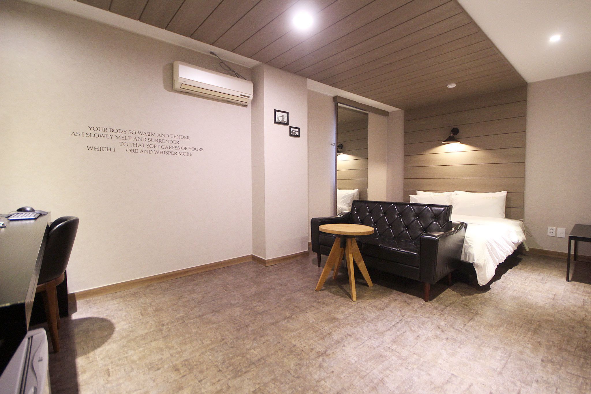 Une chambre moderne comprenant un lit, un canapé en cuir, une petite table ronde et un bureau avec un ordinateur.