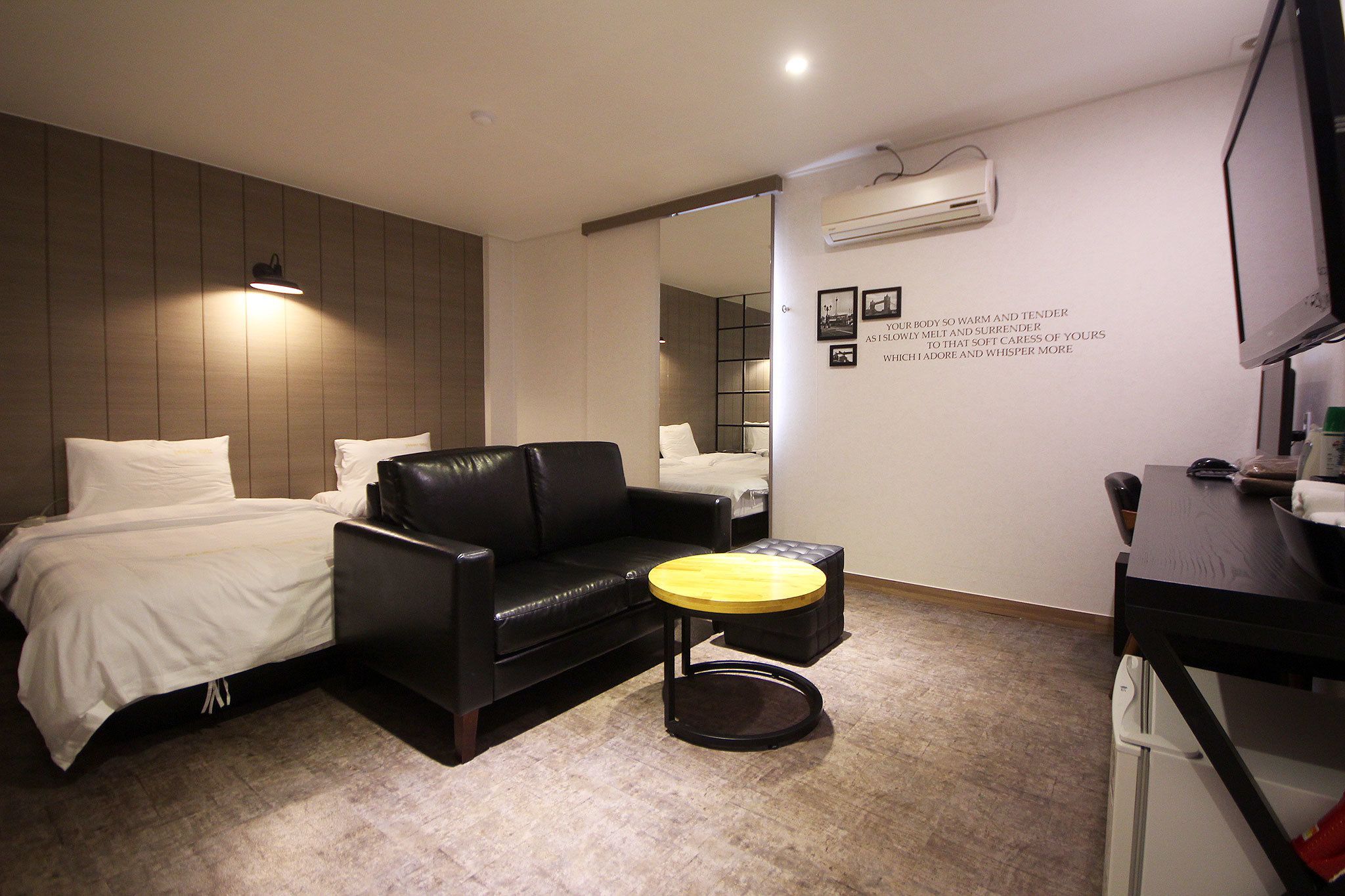 Quarto de hotel com cama, sofá de couro preto, mesa redonda pequena, espelho e ar-condicionado fixado na parede.