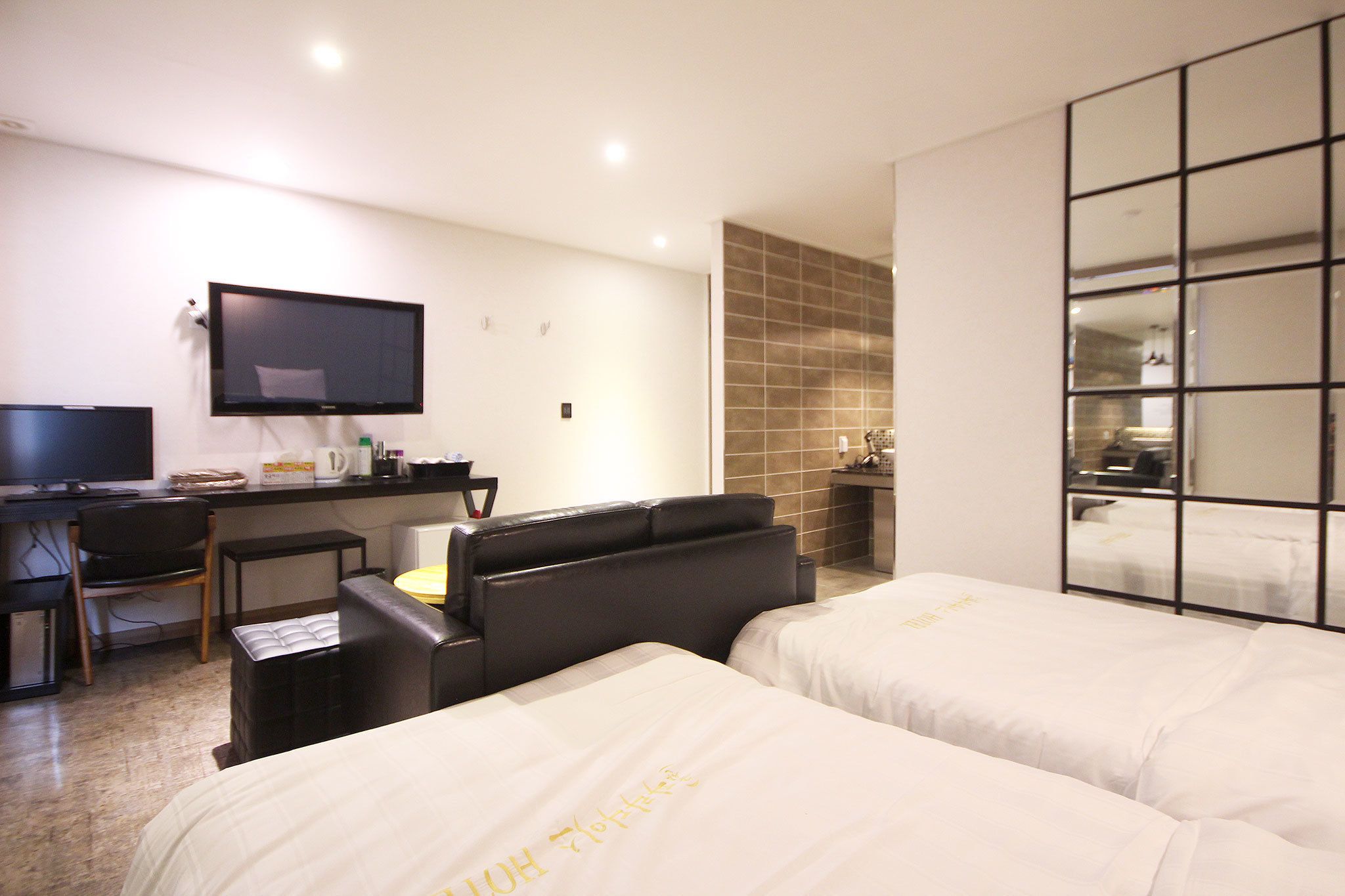 A hotel room with two beds, a desk with a computer, a TV, and a seating area.