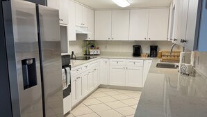 Eine moderne Küche mit weißen Schränken, einem Edelstahlkühlschrank, einer Kaffeemaschine und einem Fliesenboden.