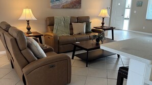 Ein Wohnzimmer mit einem braunen Ledersofa, einem Couchtisch und zwei Lampen. An der Wand hängt ein Gemälde und im Hintergrund ist eine Tür zu sehen.