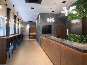 A modern bar area with a long counter, bar stools, and a green wall with a 'Cafe & Bar' sign.