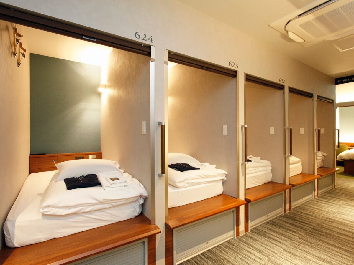 Hotellihuone, jossa on neljä sänkyä. Jokaisessa sängyssä on puinen pääty, peili ja sängyn yläpuolella oleva valaisin.