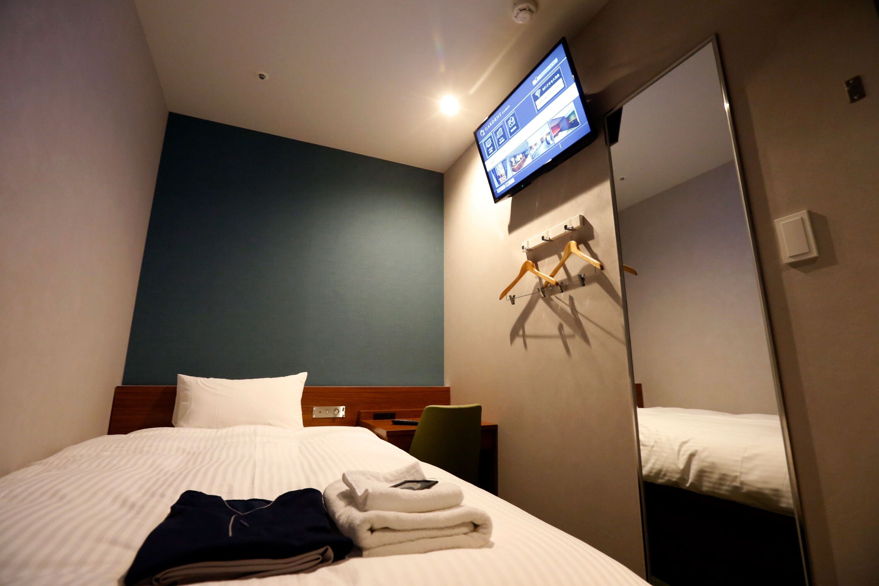 Een hotelkamer met een bed, een aan de muur bevestigde televisie, een spiegel en een kast.