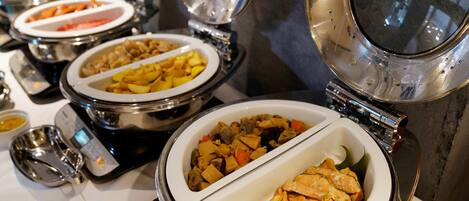 A buffet setup with multiple dishes in white and silver bowls, a weighing scale, and a steam table.