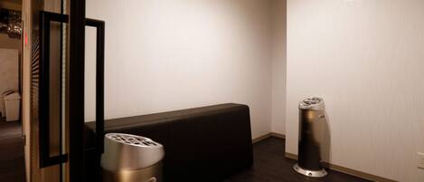 A hotel room with a dark wooden floor, a black bench, a trash bin, and a wall-mounted light fixture.