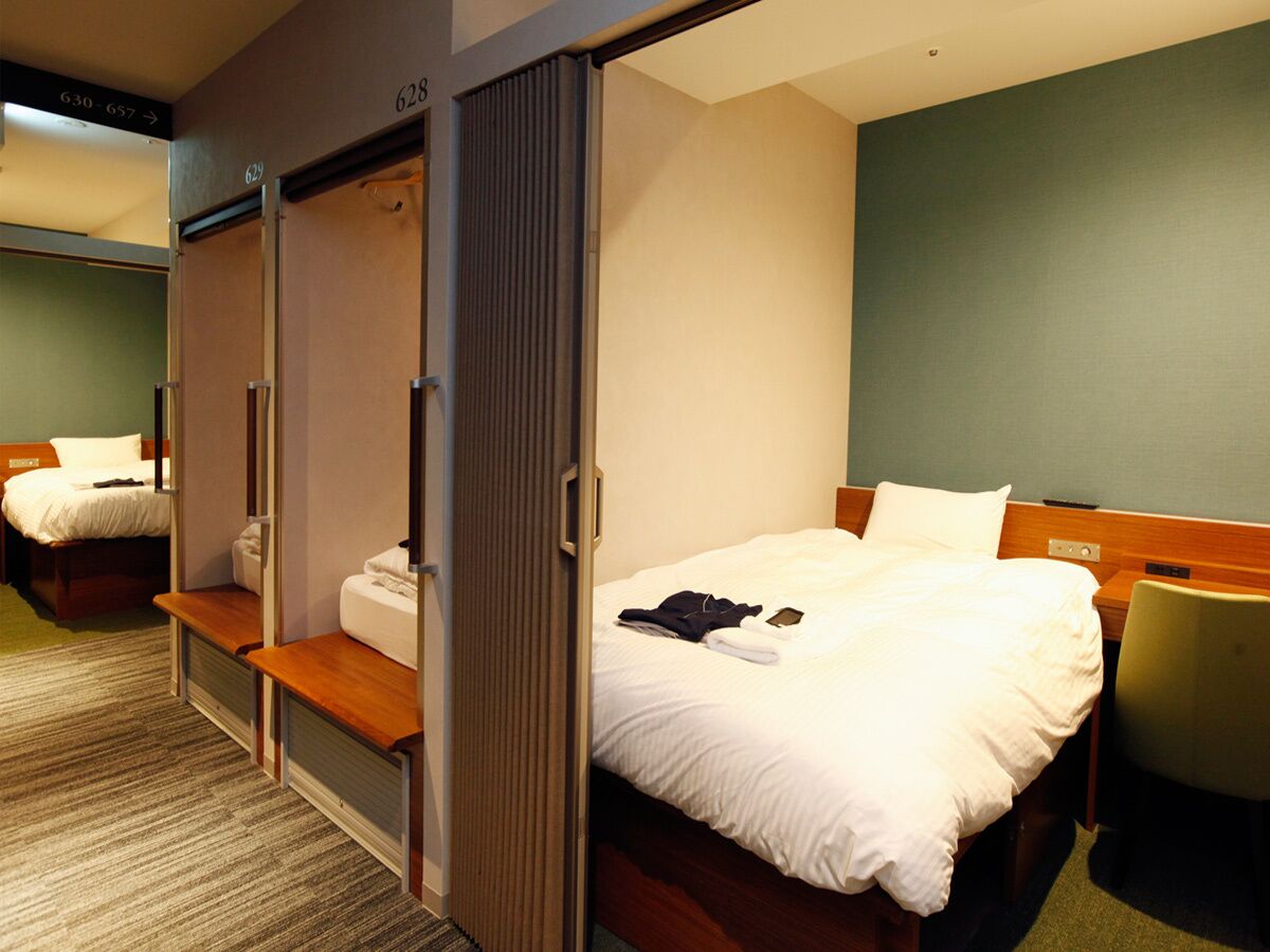 Hotellihuone, jossa on sänky, penkki, tuoli ja vaatekaappi.