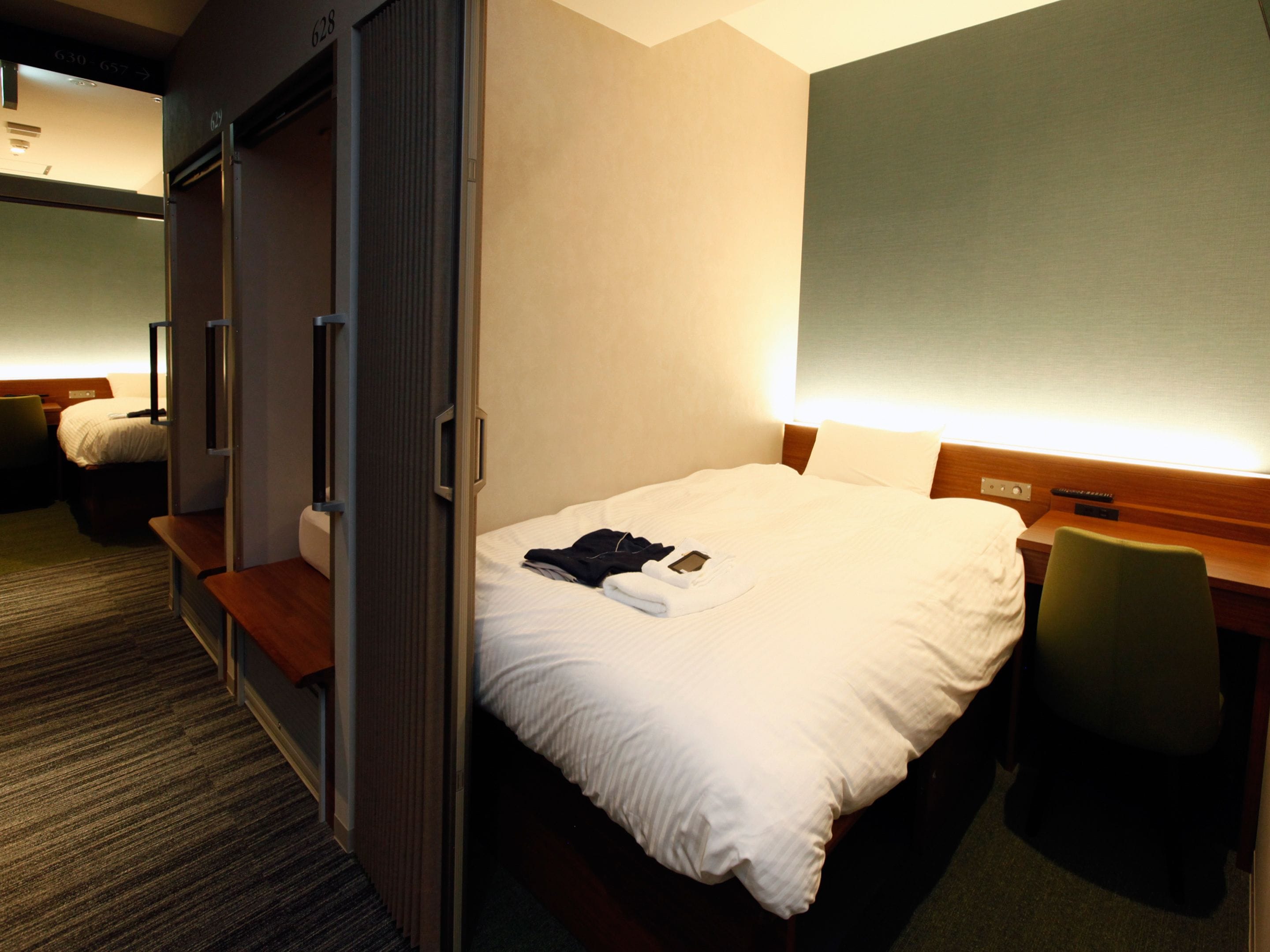 A hotel room with a bed, a desk, a chair, and a wardrobe.