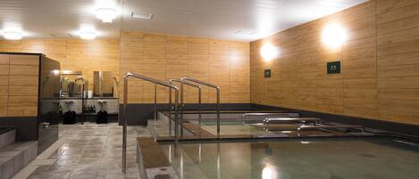Piscina interior moderna con agua cristalina, paredes de paneles de madera y barandales de metal.