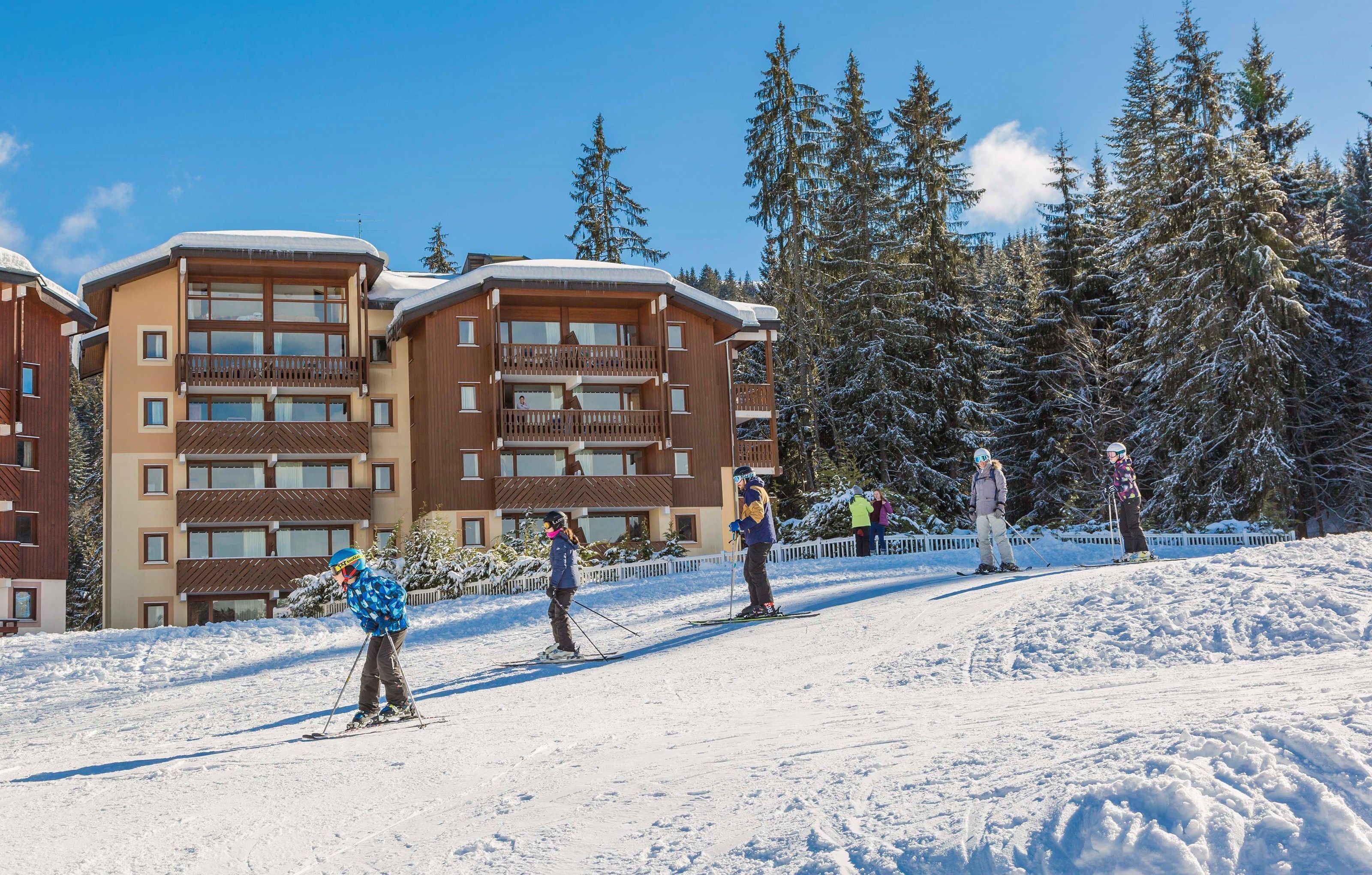 Een wintersportgebied met een meer verdiepingen tellend gebouw, skipistes en sneeuwbedekte bomen.