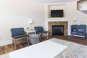 Un salon avec une cheminée, deux fauteuils, une table basse et un téléviseur fixé au mur.