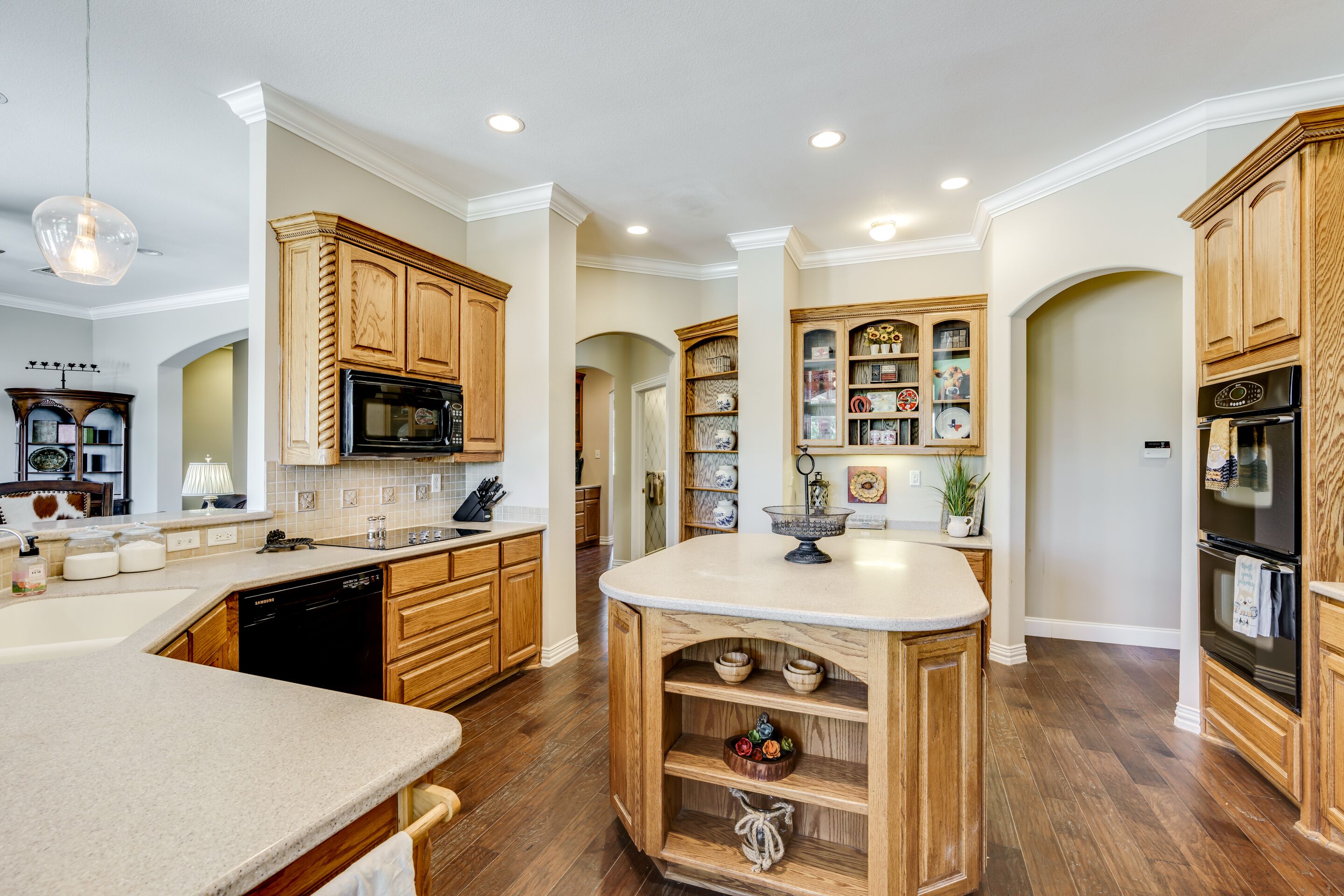 A modern kitchen with wooden cabinets, a central island, and built-in shelving.