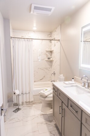 Un baño moderno con suelo de mármol, bañera, inodoro y lavabo con espejo.