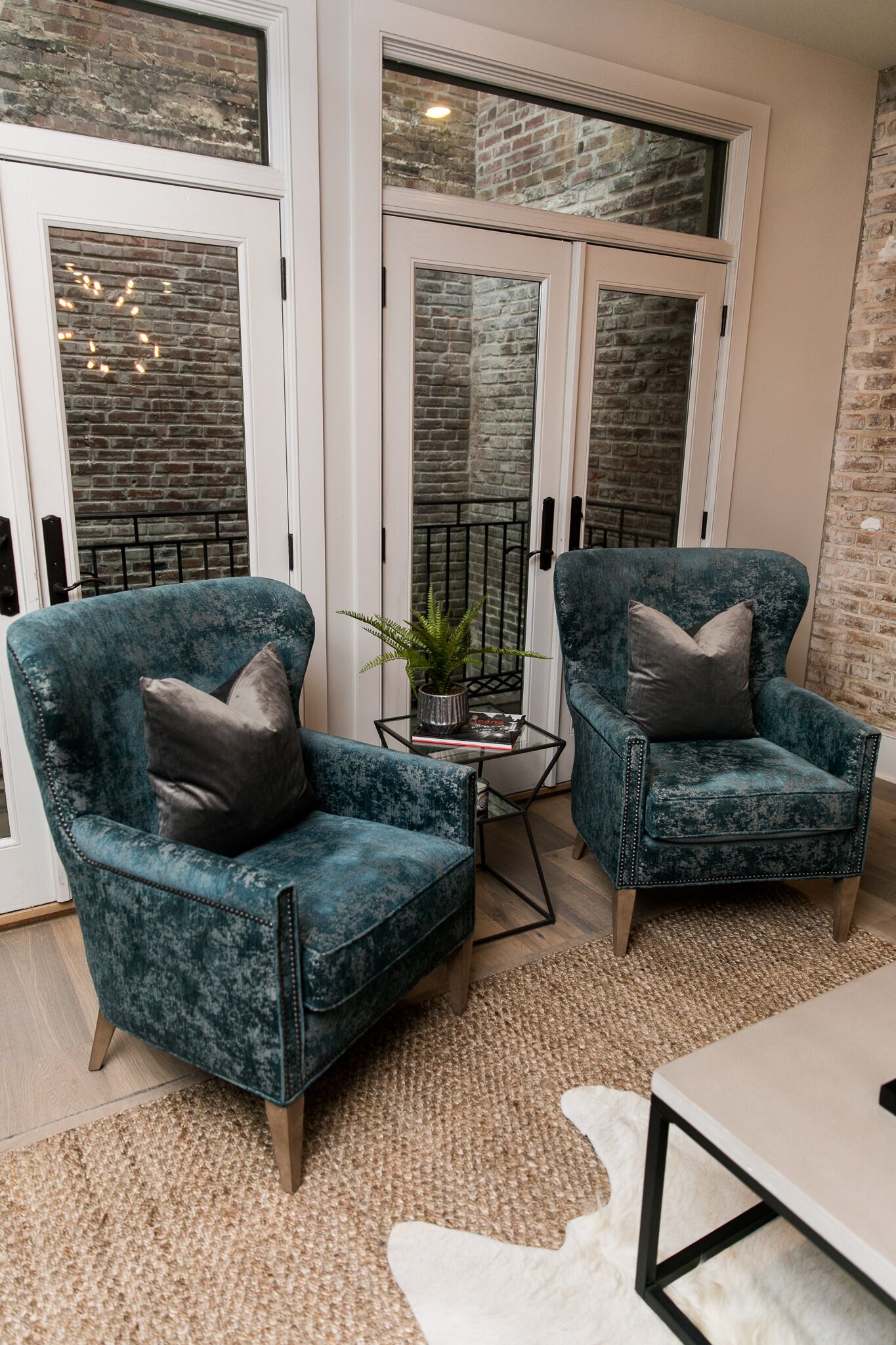 Een kamer met twee smaragdgroene fauteuils, een tafeltje met een plant en een wit vloerkleed.