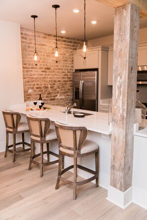 Une cuisine avec un mur en briques, des tabourets de bar en bois, un îlot en marbre et des luminaires suspendus.