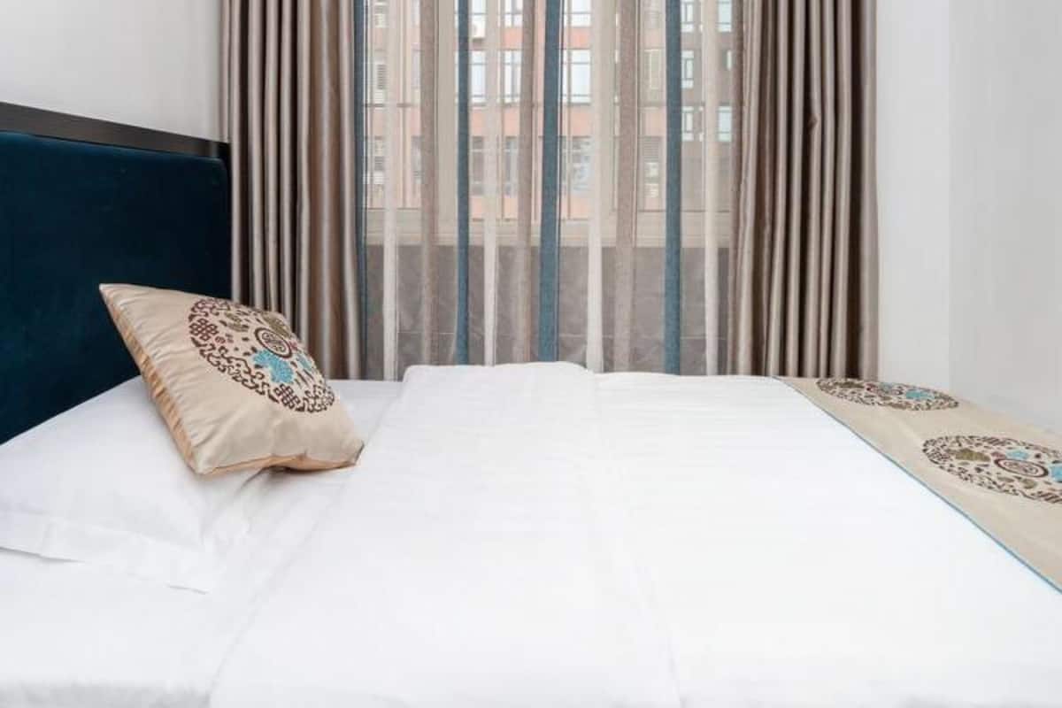 A hotel room with a bed, curtains, and a view of buildings through the window.