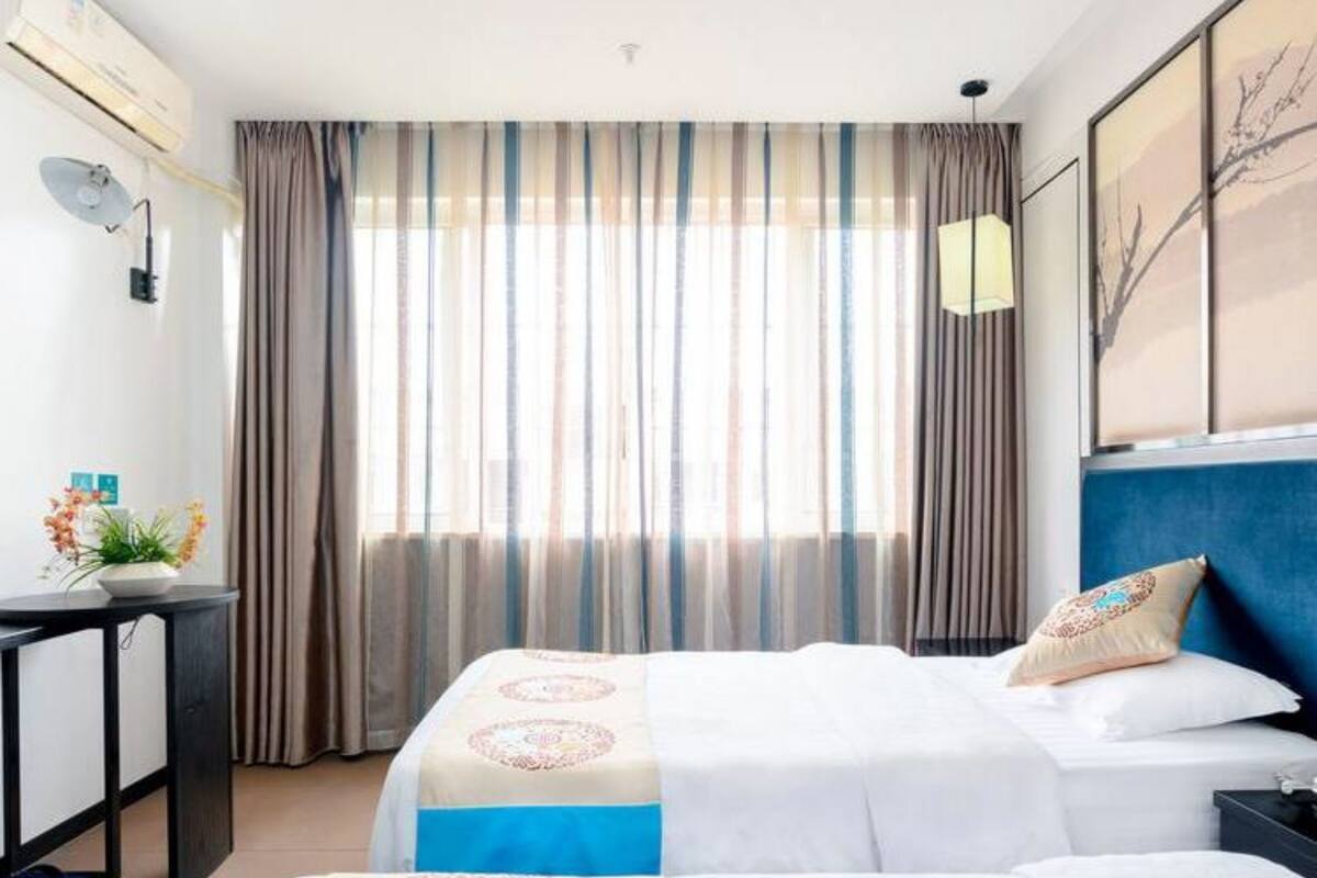 A hotel room with two beds, a desk, a chair, and a large window with curtains.