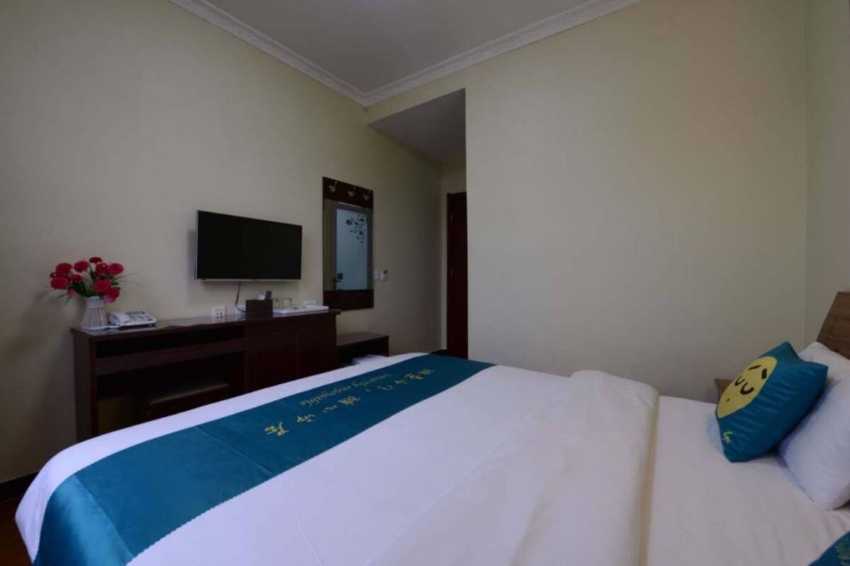 Ein Hotelzimmer mit einem Bett, einem Schreibtisch mit Telefon, einem Flachbildfernseher und einem Spiegel.