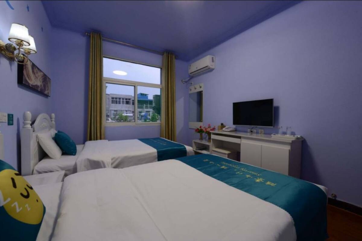 Ein Hotelzimmer mit zwei Betten, einem Schreibtisch, einem Fernseher und einem Fenster mit Vorhängen.