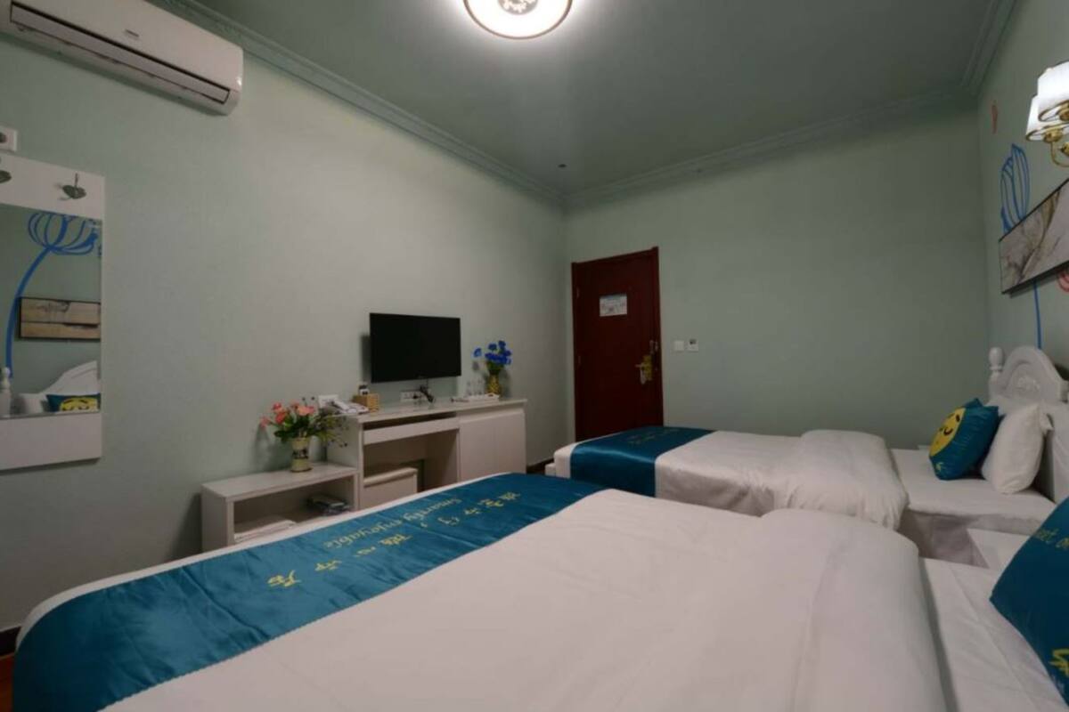 Ein Hotelzimmer mit zwei Betten, einem Schreibtisch mit Computer, einem Fernseher und einer Klimaanlage.