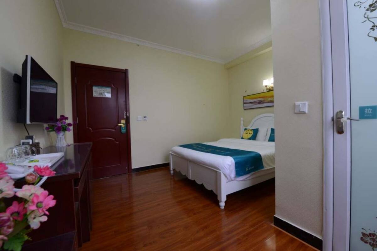 Ein Hotelzimmer mit Holzboden, einem Bett mit blauer Bettdecke, einem Schreibtisch mit Blumenvase und einem an der Wand befestigten Fernseher.