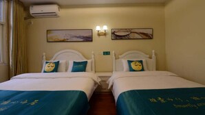 A hotel room with two beds, each with a blue bedspread and a pillow with a smiley face. There is an air conditioning unit on the wall, and two wall-mounted lamps. - Sucha Hotel Xi'an Xianyang Airport (Xianyang)