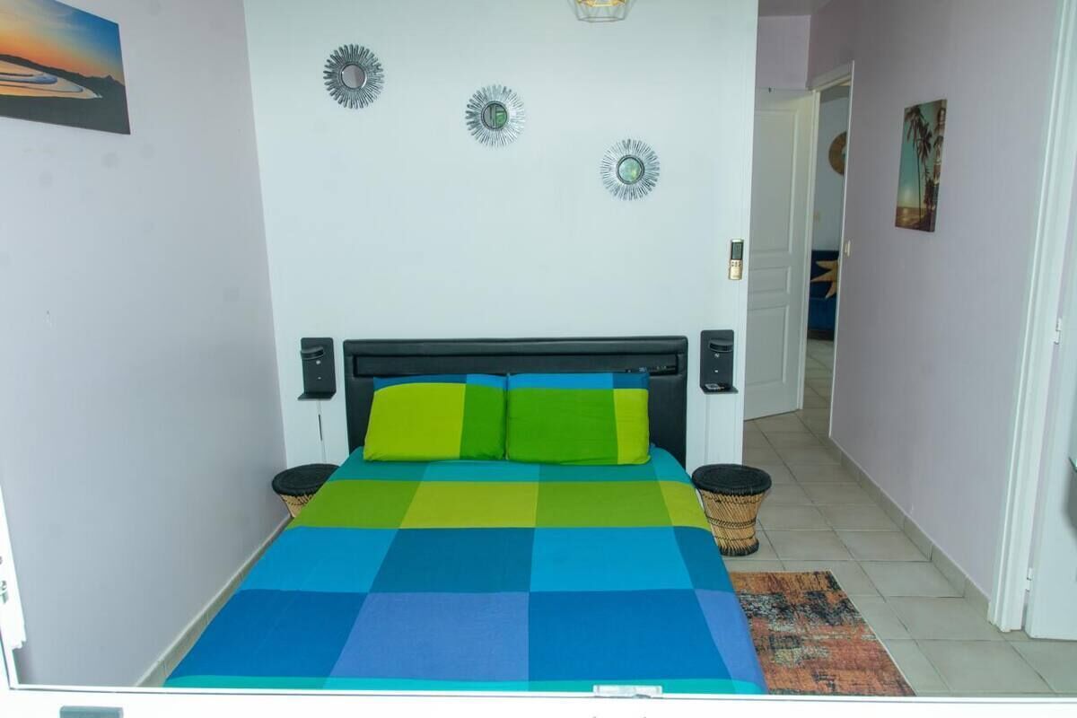 Ein Zimmer mit einem Bett, zwei Nachttischen, einer Wand mit Dekorationen und einer Tür zu einem weiteren Raum.