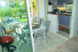 A room with a dining table, chairs, a red chair, a sofa, and a kitchen area with a microwave and sink.