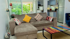 A living room with a sofa, a coffee table, and a view of the kitchen and outside.