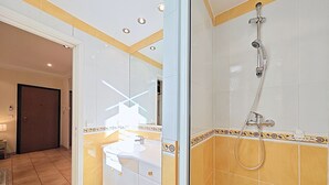 Une salle de bain avec un lavabo blanc, un miroir et une douche équipée d’un pommeau de douche amovible.