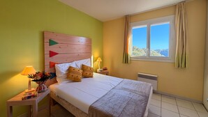 En pænt redt seng med puder, et natbord med lampe og et vindue med gardiner.