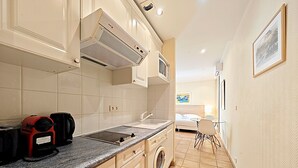 A compact kitchen with a built-in washer and dryer, a microwave, and a coffee maker. - Studio Commandant André 33 by Viva Riviera (Cannes)